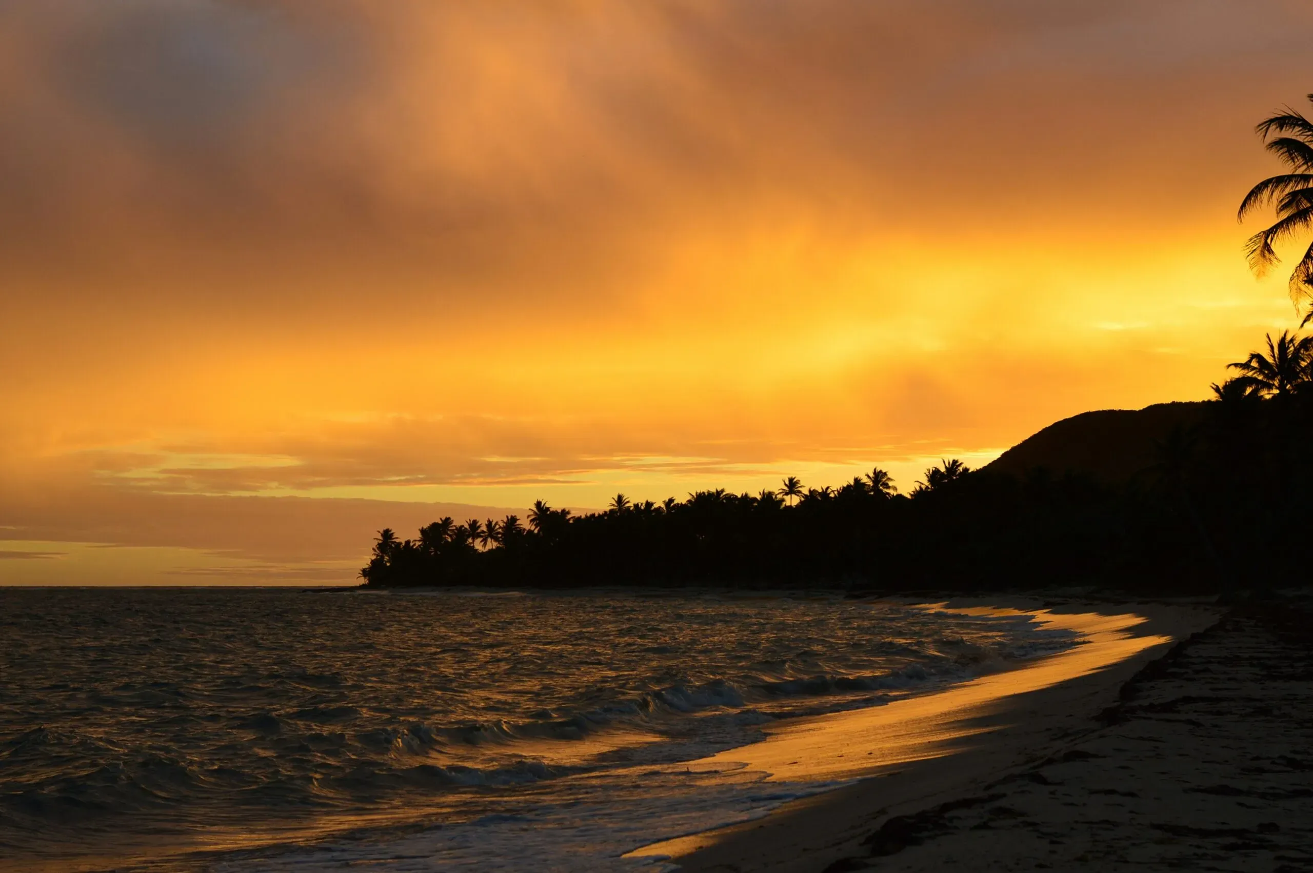 Coucher de soleil spectaculaire aux couleurs orange et jaunes sur une plage tropicale.